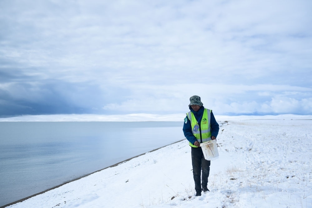 2021年10月20日，在青海省果洛藏族自治州瑪多縣扎陵湖鄉(xiāng)勒那村，三江源國家公園黃河源園區(qū)生態(tài)管護(hù)員在扎陵湖邊撿拾垃圾。新華社記者 張龍 攝