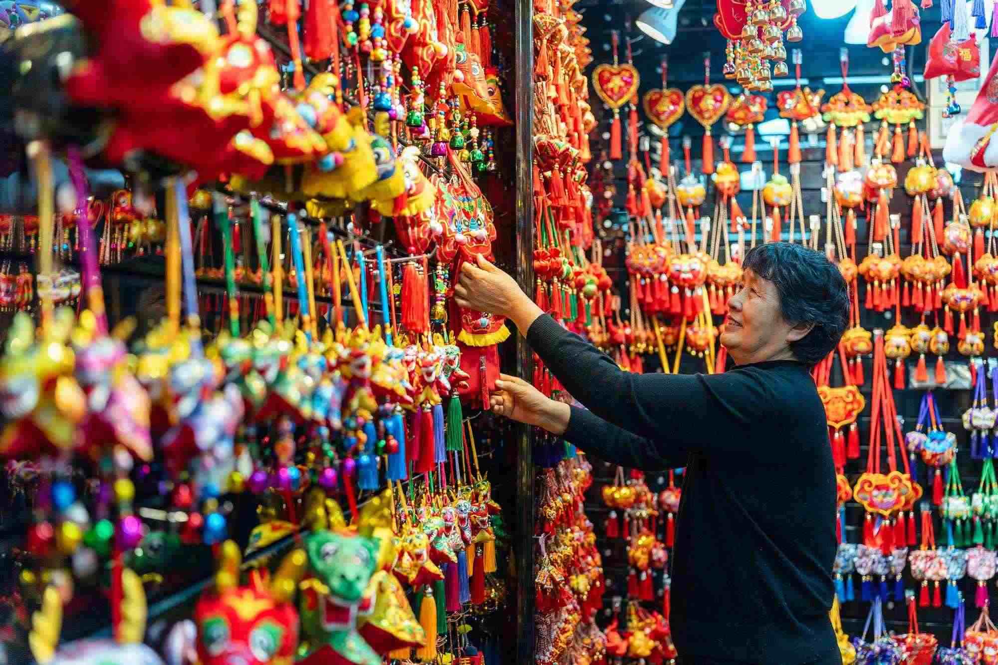 2023年12月11日，金華義烏國(guó)際商貿(mào)城，龍年喜慶用品掛滿攤位，顧客正在挑選中。