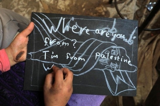 2023年12月28日，一名學生在加沙地帶南部城市拉法一所學校的臨時教室中寫下“我來自巴勒斯坦”的字樣。新華社發(fā)（里澤克·阿卜杜勒賈瓦德攝）