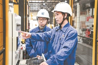在廣西柳工機(jī)械股份有限公司生產(chǎn)車(chē)間內(nèi)，一名高級(jí)技師（右）給徒弟講解數(shù)控設(shè)備操作細(xì)節(jié)。新華社記者 曹祎銘攝